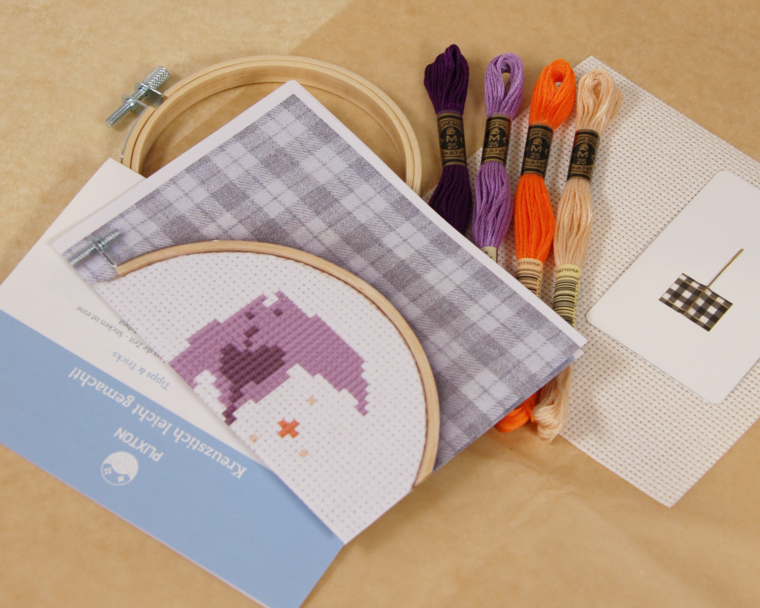 Inhalt des Ray & Sparkle Kreuzstichsets mit Stickgarn, Aida-Stoff, Stickvorlage und Holzrahmen.