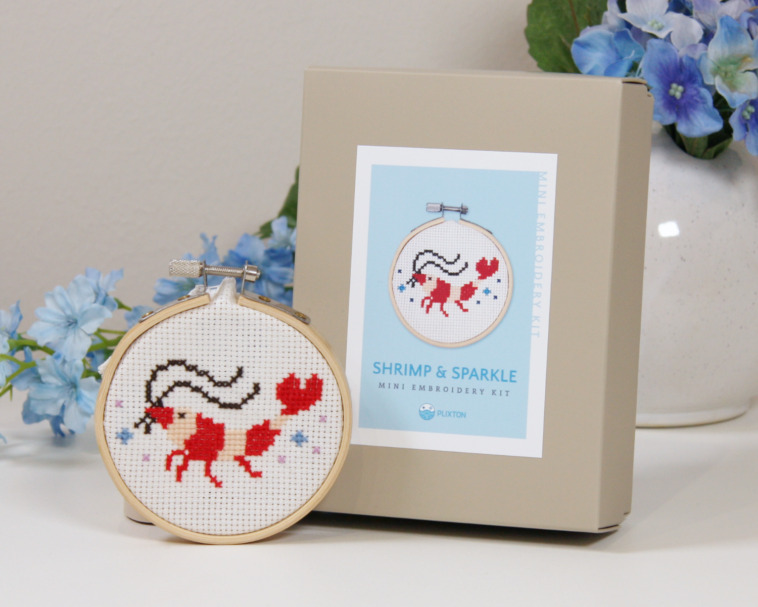 Shrimp & Sparkle Kreuzstichset mit gesticktem Garnelenmotiv im Mini-Stickrahmen.