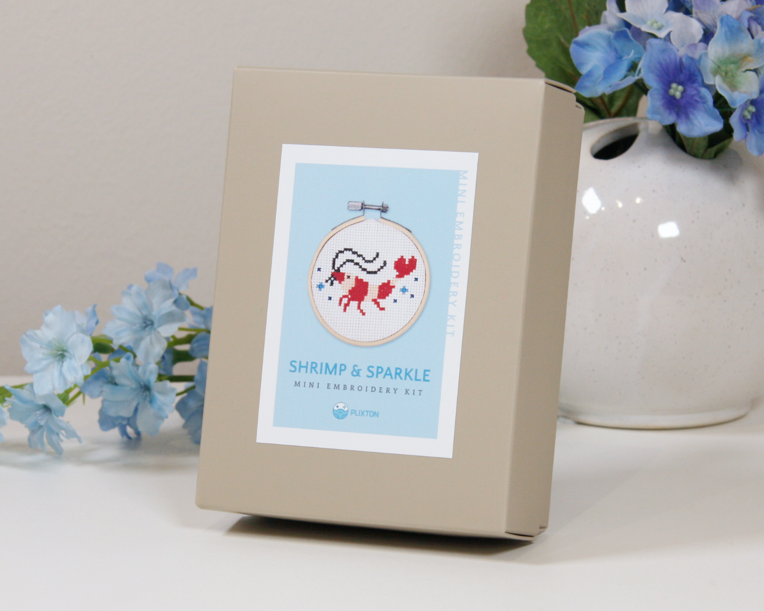 Shrimp & Sparkle Kreuzstichset mit gesticktem Garnelenmotiv im Mini-Stickrahmen.